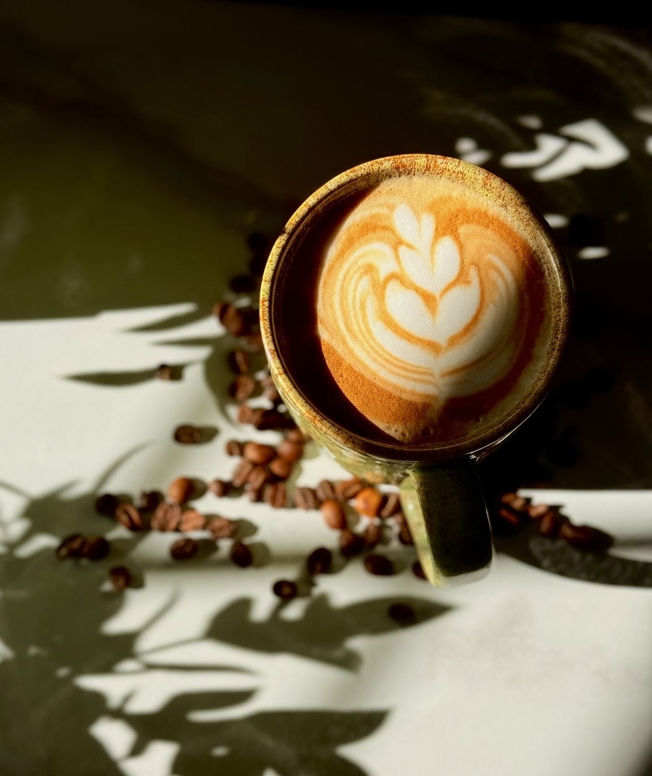 Latte art in golden light surrounded by roasted coffee beans